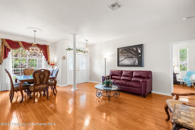 living room featuring ornate columns, a wealth of natural light, light hardwood / wood-style floors, and a notable chandelier