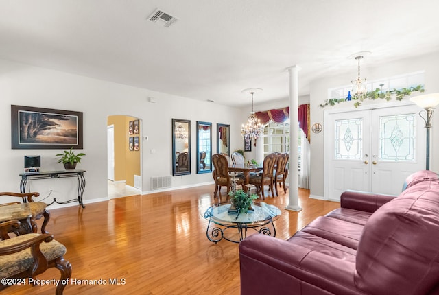 living room with french doors, light wood-type flooring, decorative columns, and an inviting chandelier