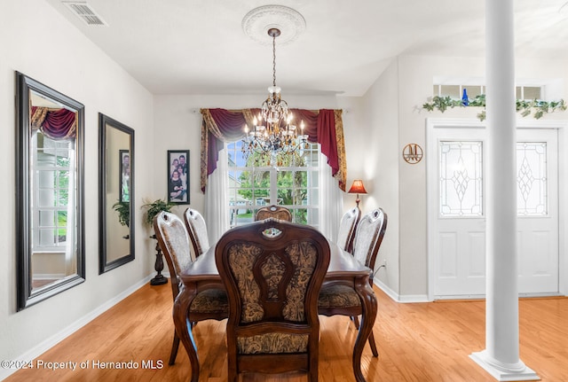 dining room featuring light wood-type flooring, ornate columns, and a notable chandelier