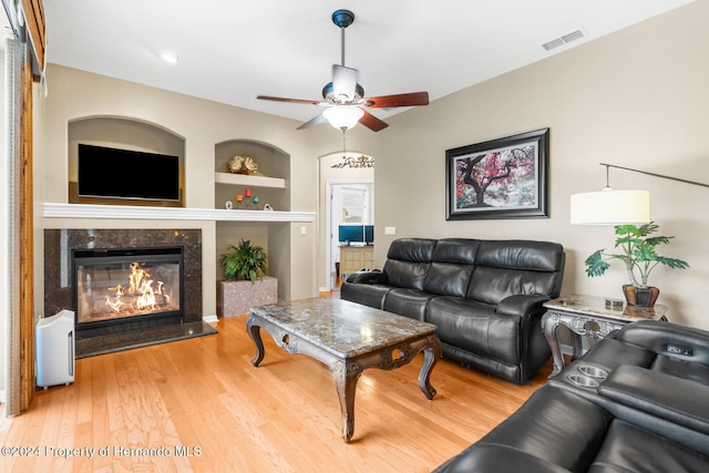 living room featuring hardwood / wood-style flooring, built in shelves, ceiling fan, and a premium fireplace