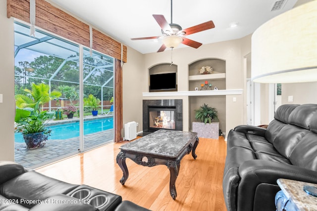 living room featuring hardwood / wood-style flooring, ceiling fan, a multi sided fireplace, and built in features