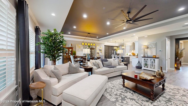 living room with light wood-type flooring, ceiling fan, crown molding, and a raised ceiling