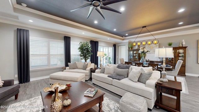 living room featuring ornamental molding, light wood-type flooring, ceiling fan, and a raised ceiling