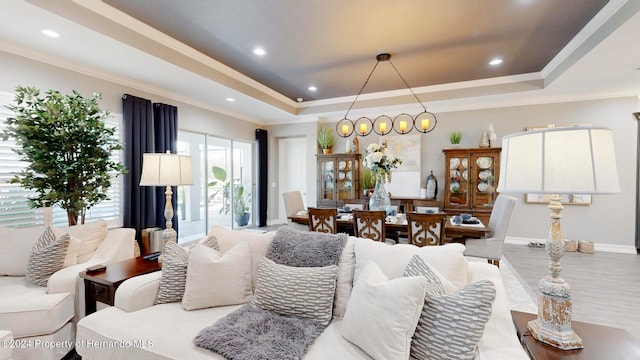 living room featuring a raised ceiling, light wood-type flooring, and ornamental molding