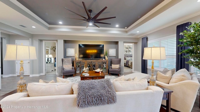 living room with ornamental molding, hardwood / wood-style floors, ceiling fan, and a raised ceiling