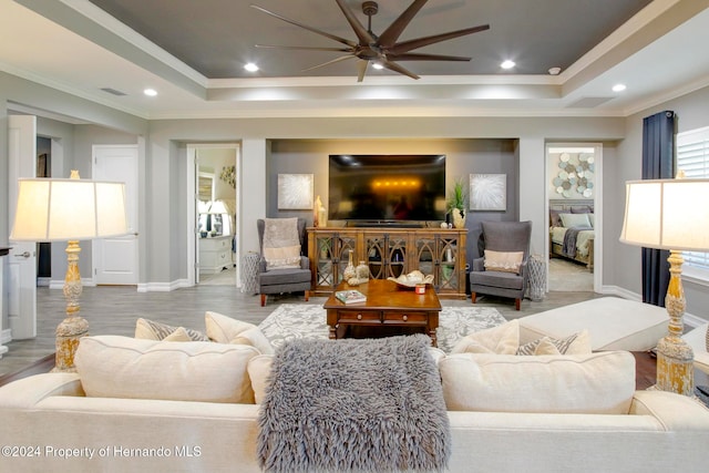 living room featuring ornamental molding, light hardwood / wood-style flooring, ceiling fan, and a tray ceiling