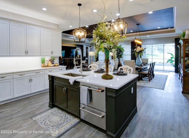 kitchen with wood-type flooring, white cabinets, hanging light fixtures, sink, and a kitchen island with sink