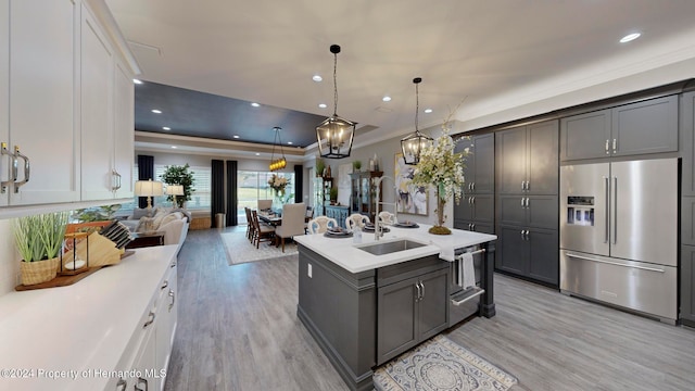 kitchen with high end fridge, a center island with sink, white cabinets, sink, and light hardwood / wood-style flooring