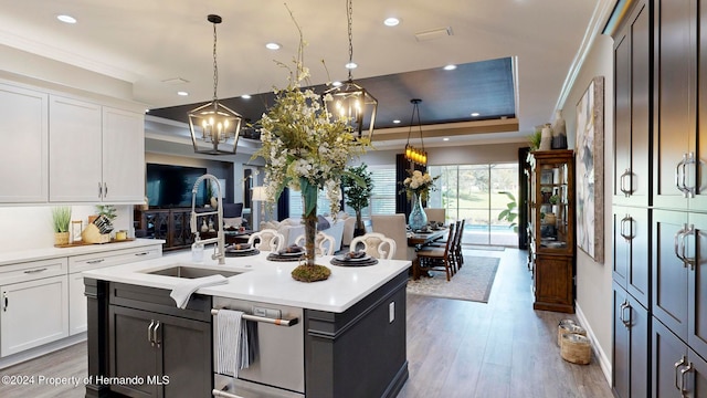 kitchen with light hardwood / wood-style flooring, white cabinetry, decorative light fixtures, and a kitchen island with sink