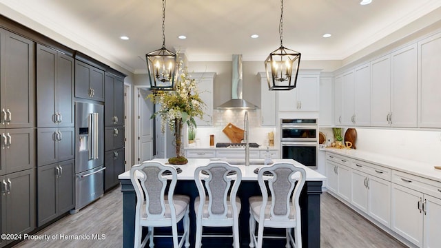 kitchen with appliances with stainless steel finishes, wall chimney exhaust hood, white cabinetry, and a kitchen island with sink