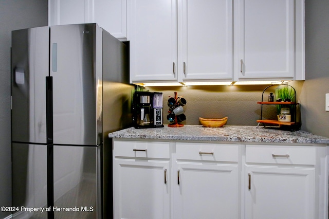 kitchen with white cabinets, stainless steel refrigerator, and light stone countertops