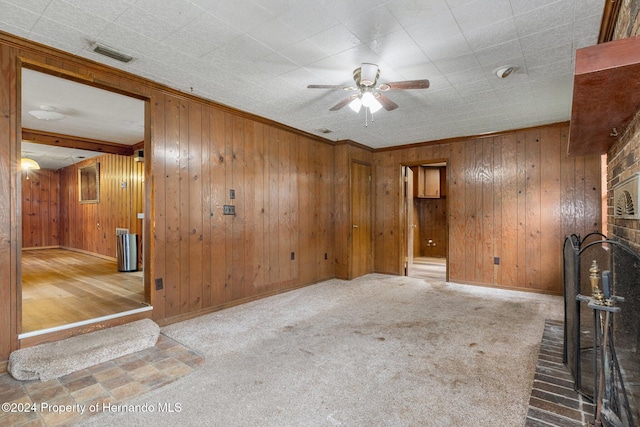 unfurnished living room with a fireplace, crown molding, carpet floors, wood walls, and ceiling fan