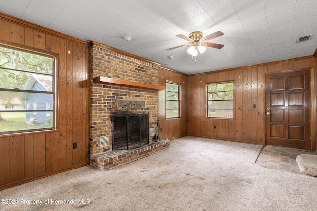 unfurnished living room featuring light colored carpet, wood walls, and a healthy amount of sunlight