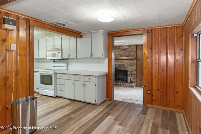 kitchen featuring hardwood / wood-style floors, white appliances, a fireplace, white cabinets, and wooden walls