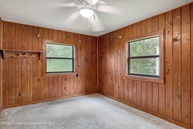 carpeted spare room featuring a wealth of natural light, wooden walls, and ceiling fan