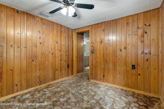 carpeted empty room with wood walls and ceiling fan