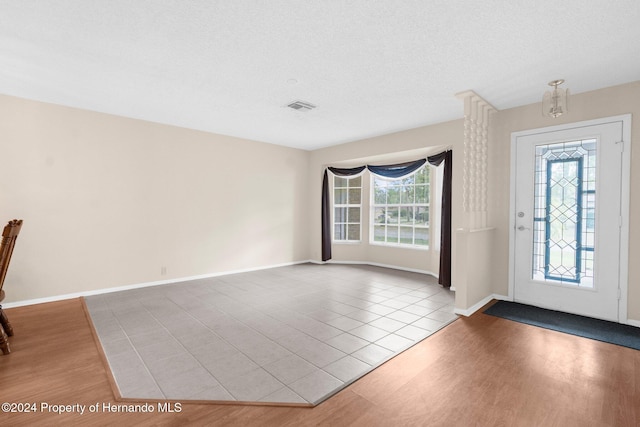 entryway with a chandelier, a textured ceiling, light wood-type flooring, and plenty of natural light