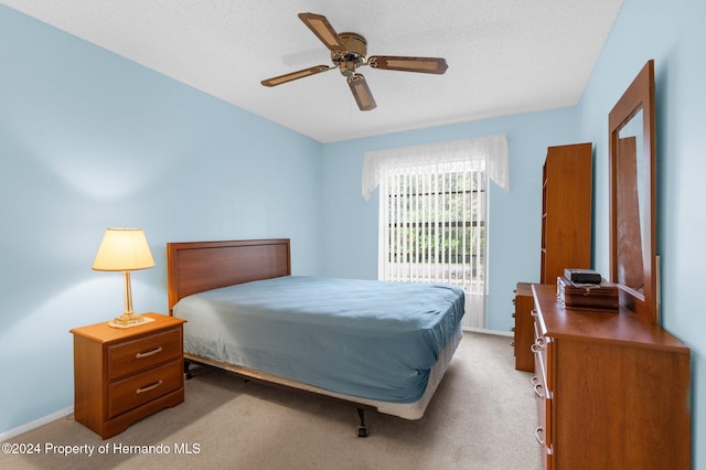 bedroom featuring ceiling fan, light colored carpet, and a textured ceiling