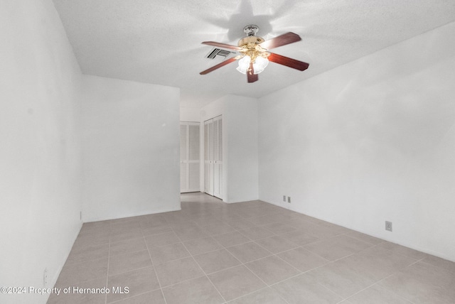 empty room featuring ceiling fan, light tile patterned floors, and a textured ceiling