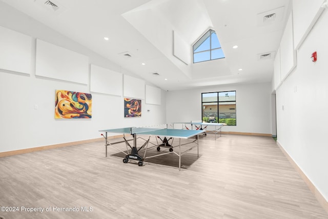 game room featuring a towering ceiling and light wood-type flooring