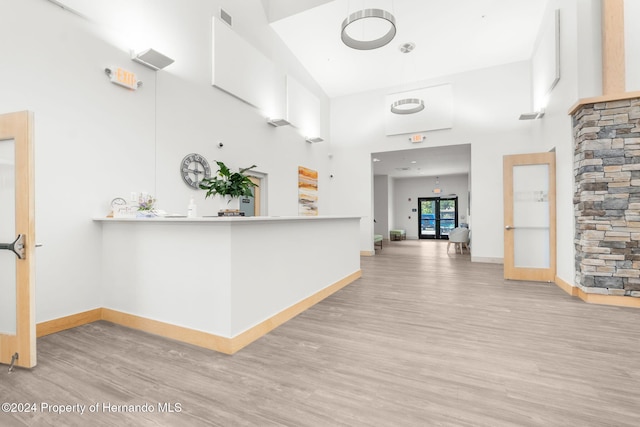 corridor with french doors, a towering ceiling, and light hardwood / wood-style floors