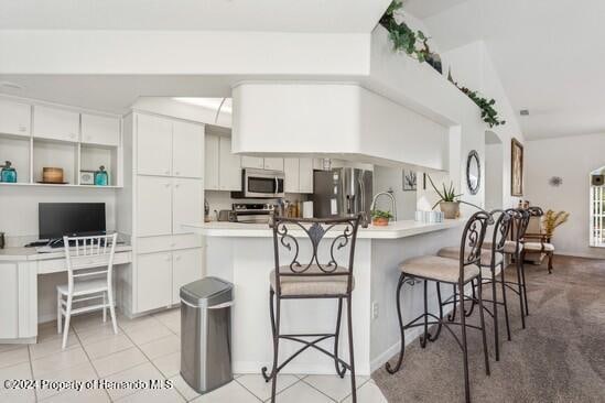 kitchen with kitchen peninsula, white cabinets, stainless steel appliances, and vaulted ceiling