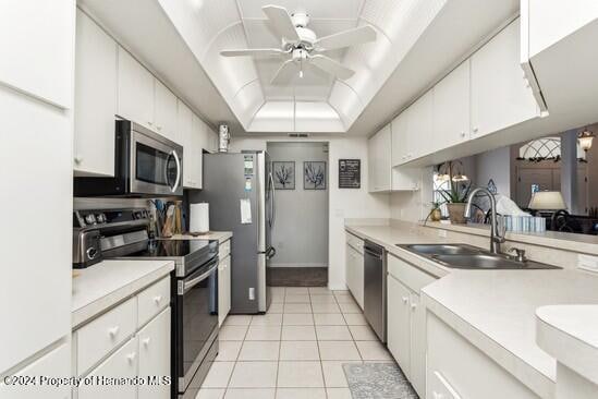 kitchen with sink, light tile patterned flooring, a tray ceiling, white cabinets, and appliances with stainless steel finishes