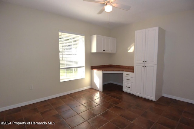 unfurnished office featuring ceiling fan, dark tile patterned floors, and built in desk