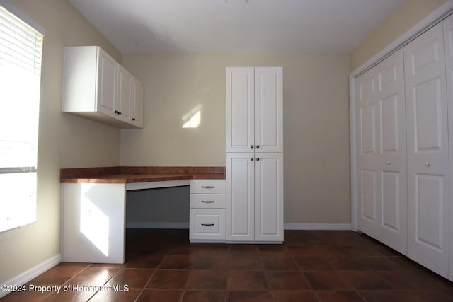 unfurnished office with dark tile patterned floors and built in desk