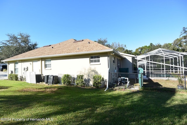 rear view of house with a lawn, glass enclosure, and central AC unit