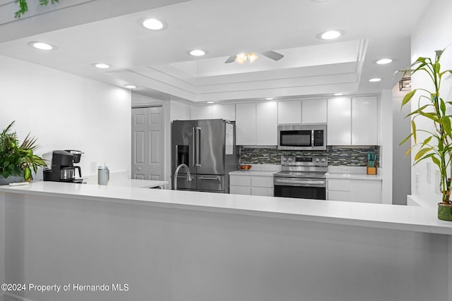 kitchen featuring white cabinets, tasteful backsplash, ceiling fan, a raised ceiling, and appliances with stainless steel finishes