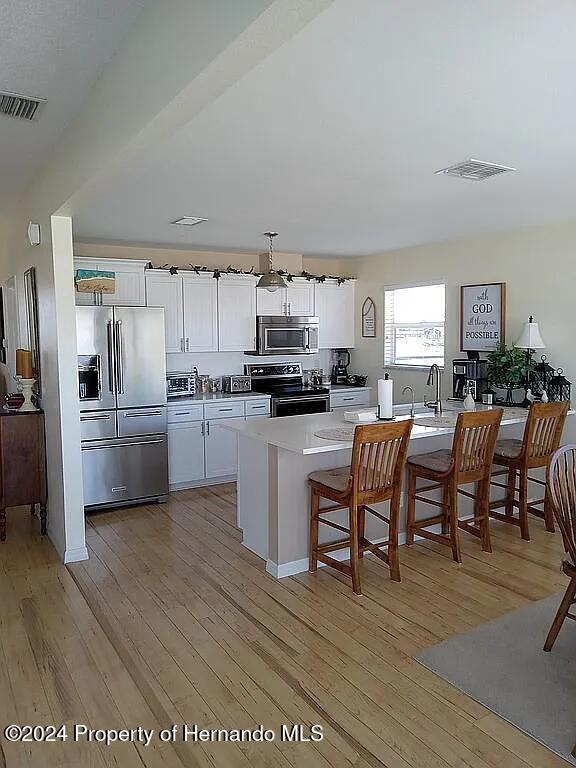 kitchen with white cabinetry, appliances with stainless steel finishes, a breakfast bar area, and light hardwood / wood-style flooring