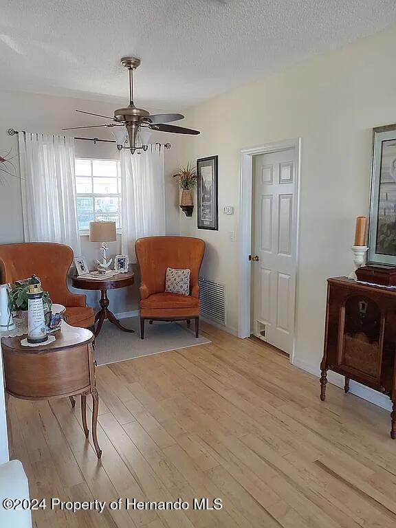 living area featuring a textured ceiling, ceiling fan, and light hardwood / wood-style flooring