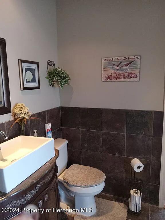 bathroom with toilet, vanity, and tile walls