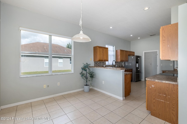 kitchen with kitchen peninsula, hanging light fixtures, sink, backsplash, and stainless steel fridge