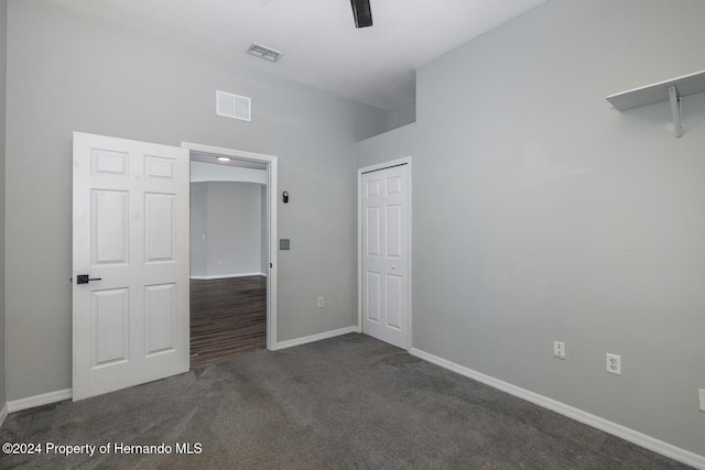 unfurnished bedroom with ceiling fan, dark colored carpet, a closet, and vaulted ceiling