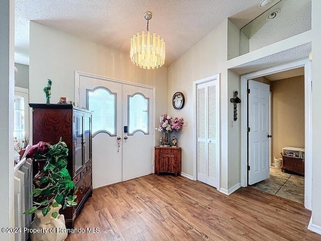 entryway featuring french doors, wood-type flooring, a textured ceiling, a notable chandelier, and vaulted ceiling