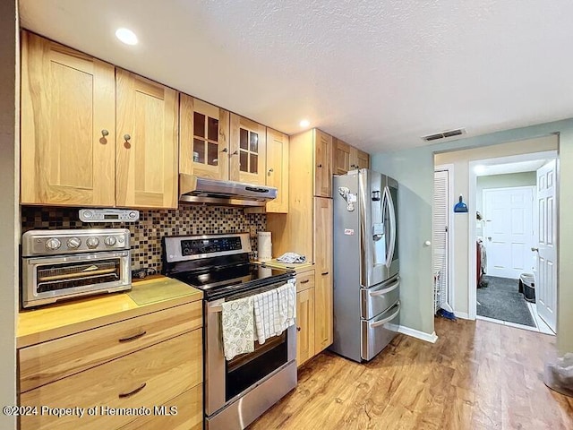 kitchen with light brown cabinets, appliances with stainless steel finishes, exhaust hood, and light hardwood / wood-style flooring