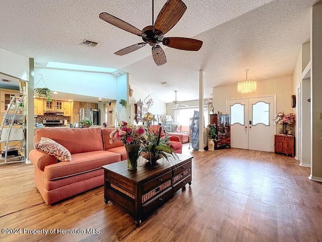 living room with ceiling fan with notable chandelier, lofted ceiling, a textured ceiling, and wood-type flooring