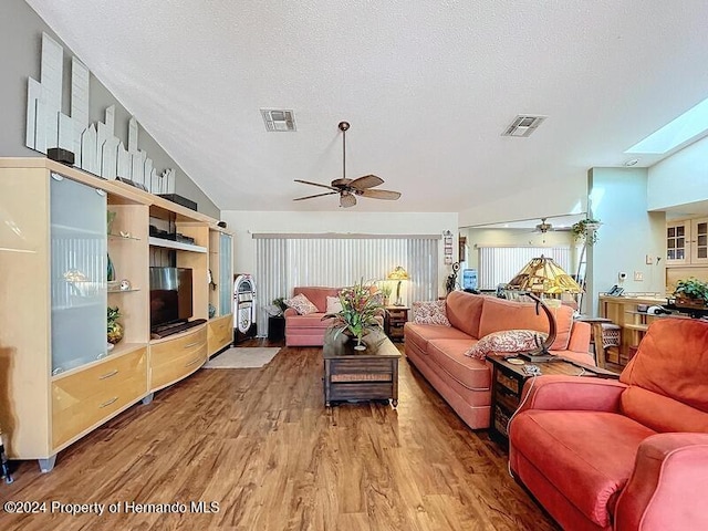 living room featuring ceiling fan, vaulted ceiling with skylight, wood-type flooring, and a textured ceiling