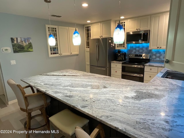 kitchen featuring tasteful backsplash, stainless steel appliances, pendant lighting, a breakfast bar, and white cabinets