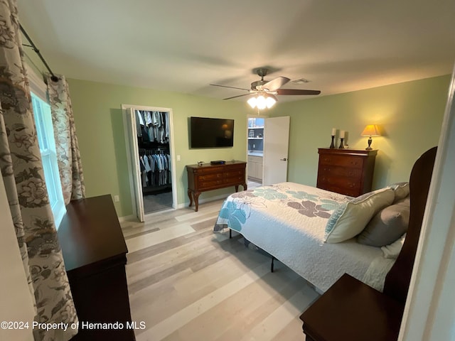 bedroom featuring a closet, light wood-type flooring, a walk in closet, and ceiling fan