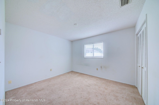 unfurnished bedroom with a closet, light colored carpet, and a textured ceiling