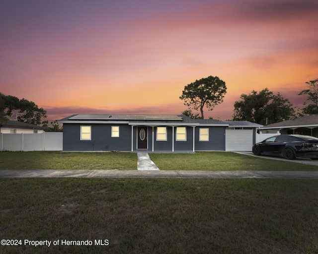 single story home with solar panels, a garage, and a yard