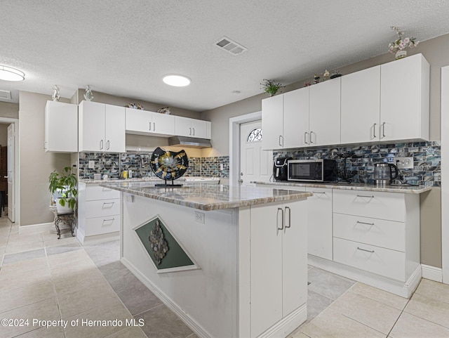 1009 Cobbelstone Dr, Spring Hill, FL 34606 - kitchen with stainless steel microwave, a center island, tasteful backsplash, white cabinetry, and light stone counters