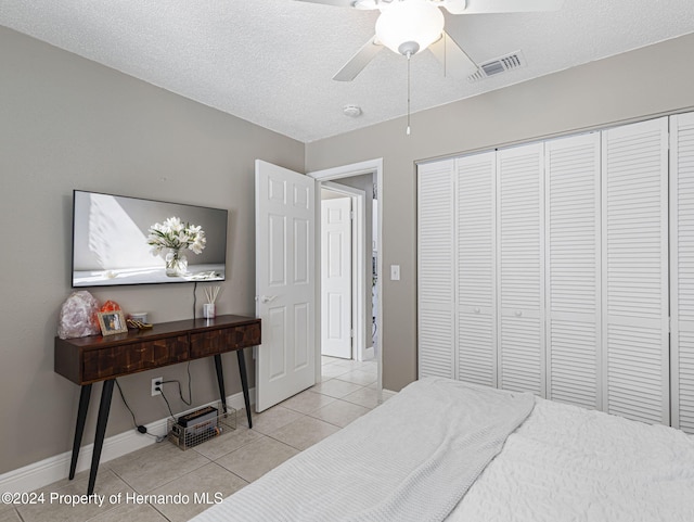 tiled bedroom with a textured ceiling, ceiling fan, and a closet