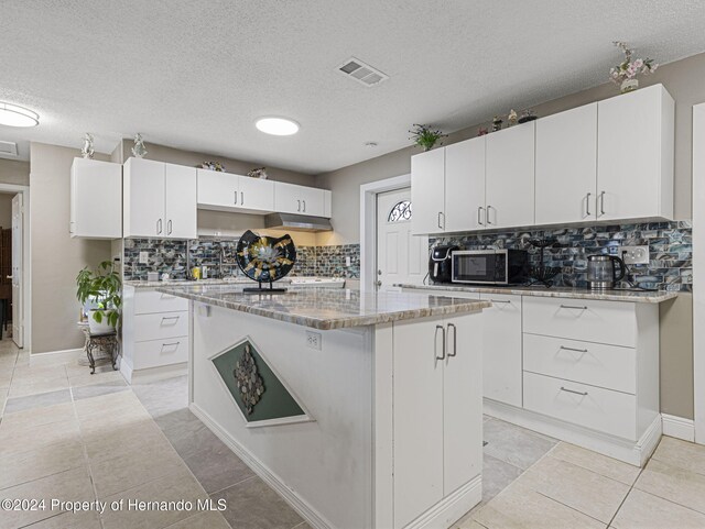 1009 Cobbelstone Dr, Spring Hill, FL 34606 - kitchen with stainless steel microwave, a center island, tasteful backsplash, white cabinetry, and light stone counters