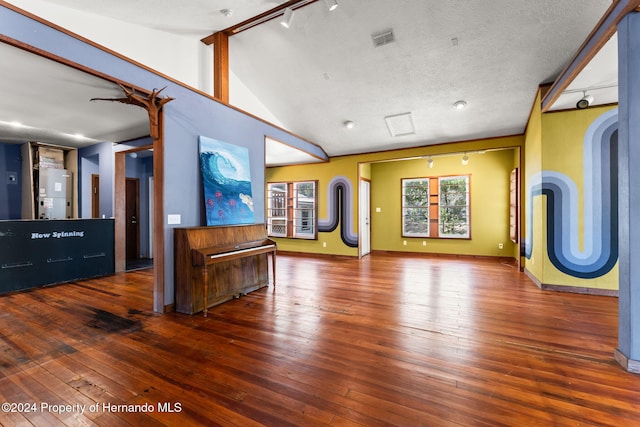 unfurnished living room with a textured ceiling, hardwood / wood-style floors, track lighting, and lofted ceiling