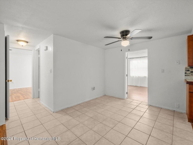 empty room with a textured ceiling, light tile patterned floors, and ceiling fan