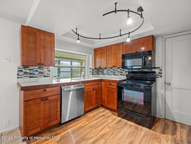 kitchen featuring black appliances, backsplash, a textured ceiling, a tray ceiling, and light hardwood / wood-style flooring